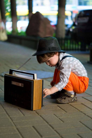 A young boy crouching and adjusting the dial on a vintage transistor radio.