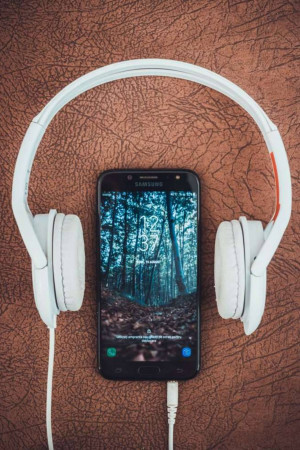 White headphones lying on top of a smartphone with a forest wallpaper