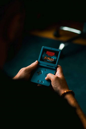Hands holding a blue Game Boy Advance SP playing a Stranger Things game.