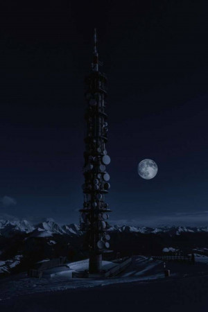 A tall communication tower silhouetted against a full moon and a dark night sky.