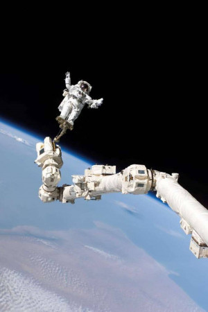 Astronaut performing a spacewalk attached to a robotic arm with Earth in the background