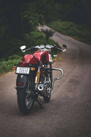 Rear view of a red Royal Enfield Continental GT motorcycle on a paved mountain road.
