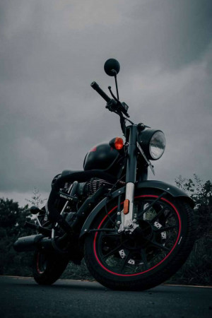Black Royal Enfield motorcycle parked on a road under a cloudy sky