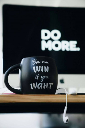 Black coffee mug with motivational text in front of a computer screen.