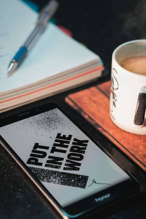 Smartphone with motivational text, coffee, pen and notebook on a wooden surface