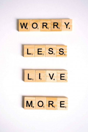 Wooden Scrabble tiles spelling out 'Worry Less, Live More' on a white background.