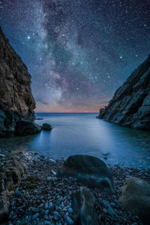 Night landscape of a rocky coastline under a vibrant Milky Way galaxy