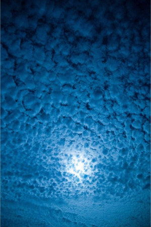 A view looking up at a cloudy night sky with a bright moon.