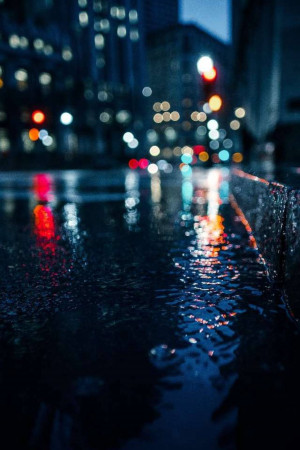 A wet city street at night with blurred lights reflecting in puddles.