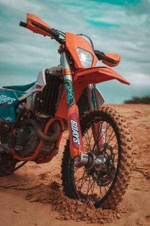 Close-up of an orange dirt bike parked on sandy terrain