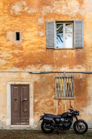 A weathered orange building facade with a window, door, and a parked motorcycle.