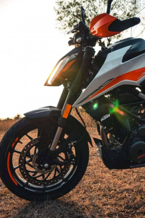 Close-up of an orange and white KTM Duke motorcycle with a blurred sunset background.