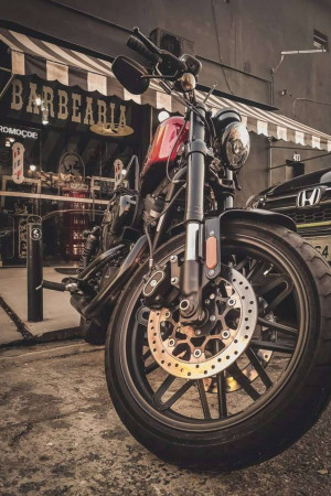 Close-up of a red and black Harley Davidson motorcycle parked in front of a barbershop.