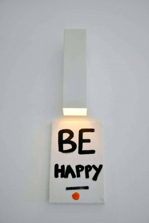 White wall with a rectangular art piece displaying the words 'BE HAPPY' in black lettering and an orange dot.