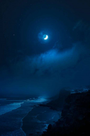 Crescent moon over a dark ocean and cloudy sky