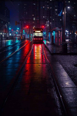 A tram traveling down a wet city street at night, illuminated by red and blue lights.