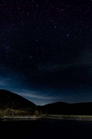 A breathtaking view of a starry night sky over a silhouetted mountain range and lake.