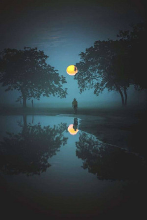 A lone figure stands before a large, bright moon reflected in water.