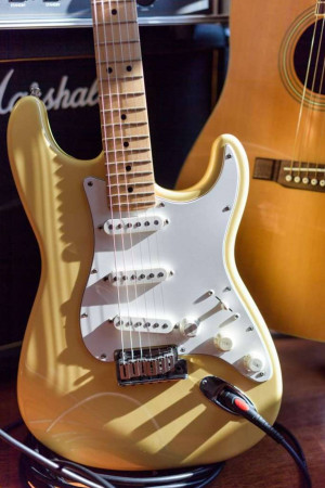 Close-up of a yellow electric guitar with a Marshall amplifier and an acoustic guitar in the background.
