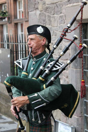 A man playing the bagpipes in a green and tartan uniform.