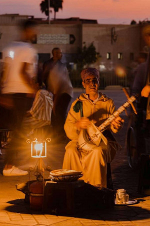 A Moroccan man playing a traditional stringed instrument in a dimly lit square.