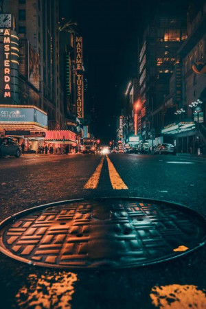 Night view of a street in Amsterdam with a manhole cover in the foreground