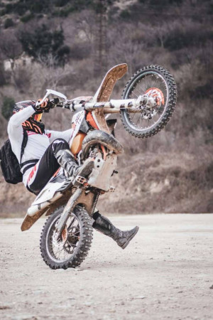 A motocross rider performing a wheelie on a dirt bike.