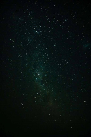 A dark night sky filled with stars and the faint glow of the Milky Way galaxy.
