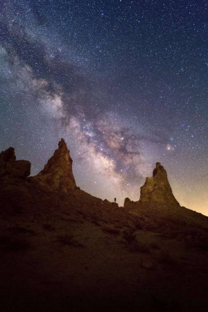 Night landscape with the Milky Way galaxy over unique rock formations and a silhouetted person.