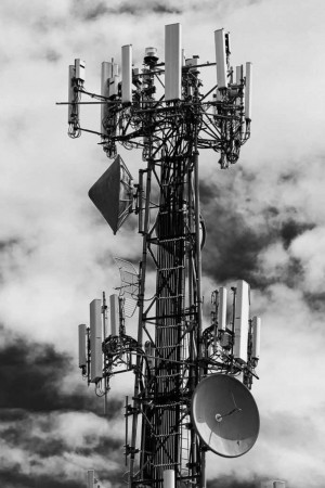 Black and white image of a tall cell tower against a cloudy sky