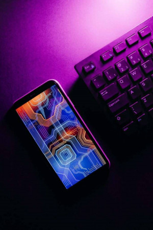 Smartphone displaying circuit board design next to a computer keyboard with neon lighting.