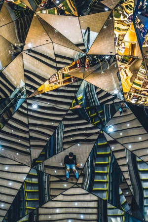 A person standing on stairs surrounded by a mirrored ceiling creating an infinite reflection effect.