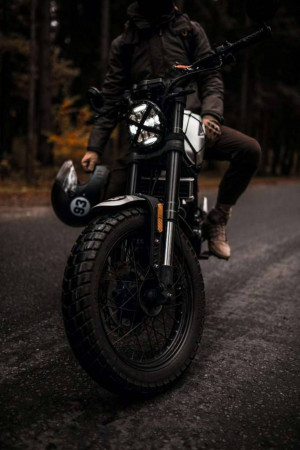 A person sitting on a custom cafe racer motorcycle on a paved road.