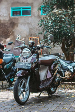 Close-up of a purple Yamaha scooter parked on a brick driveway in Indonesia.