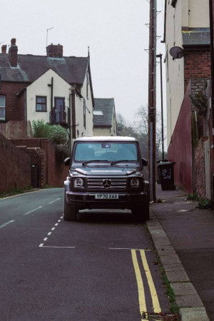 Front view of a grey Mercedes-Benz G-Wagon parked on a narrow street with brick buildings.