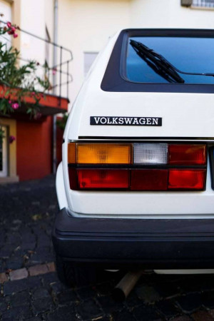 Rear view of a classic white Volkswagen Golf parked on a cobblestone driveway.