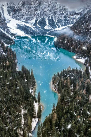 Aerial view of a turquoise lake surrounded by snow-covered mountains and pine trees.
