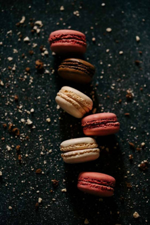 A close-up shot of a row of colorful macarons on a dark speckled surface.