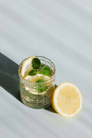 A glass of lemon and mint infused water with a lemon slice beside it.