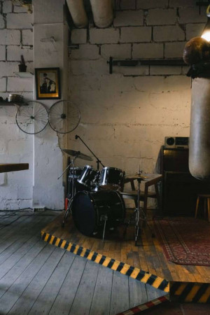 A drum set on a small stage in a room with exposed brick and industrial elements.