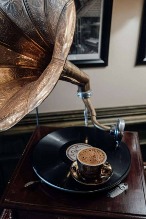 A vintage gramophone with a vinyl record, a cup of coffee, and a small plate.
