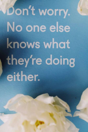 Close-up of a card with the quote 'Don't worry. No one else knows what they're doing either.' surrounded by white flowers.