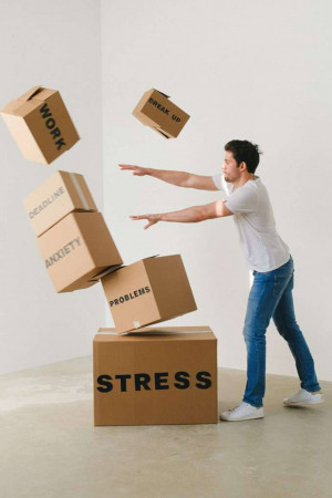 Man struggling to hold up falling boxes labeled with stress-related words.