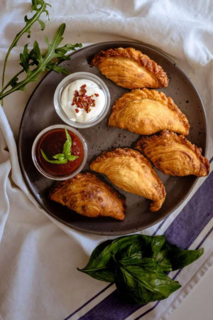 Overhead shot of golden brown empanadas served with a side of sour cream and chili sauce.