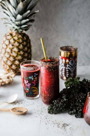 Close-up of a vibrant red beet and pineapple smoothie in a glass with a golden straw, garnished with kale and chia seeds.