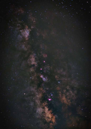 A stunning vertical view of the Milky Way galaxy with vibrant pink and brown nebulas against a dark starry sky.