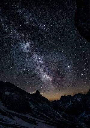 Night sky with the Milky Way galaxy visible over a silhouetted mountain range.