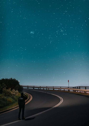 Silhouette of a person with a camera on a winding road under a starry night sky.