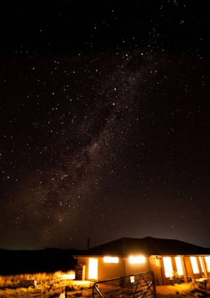 Night sky with the Milky Way galaxy visible above a lit building in a rural landscape.