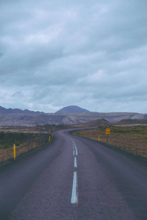 A winding asphalt road through a desolate, rocky landscape in Iceland.
